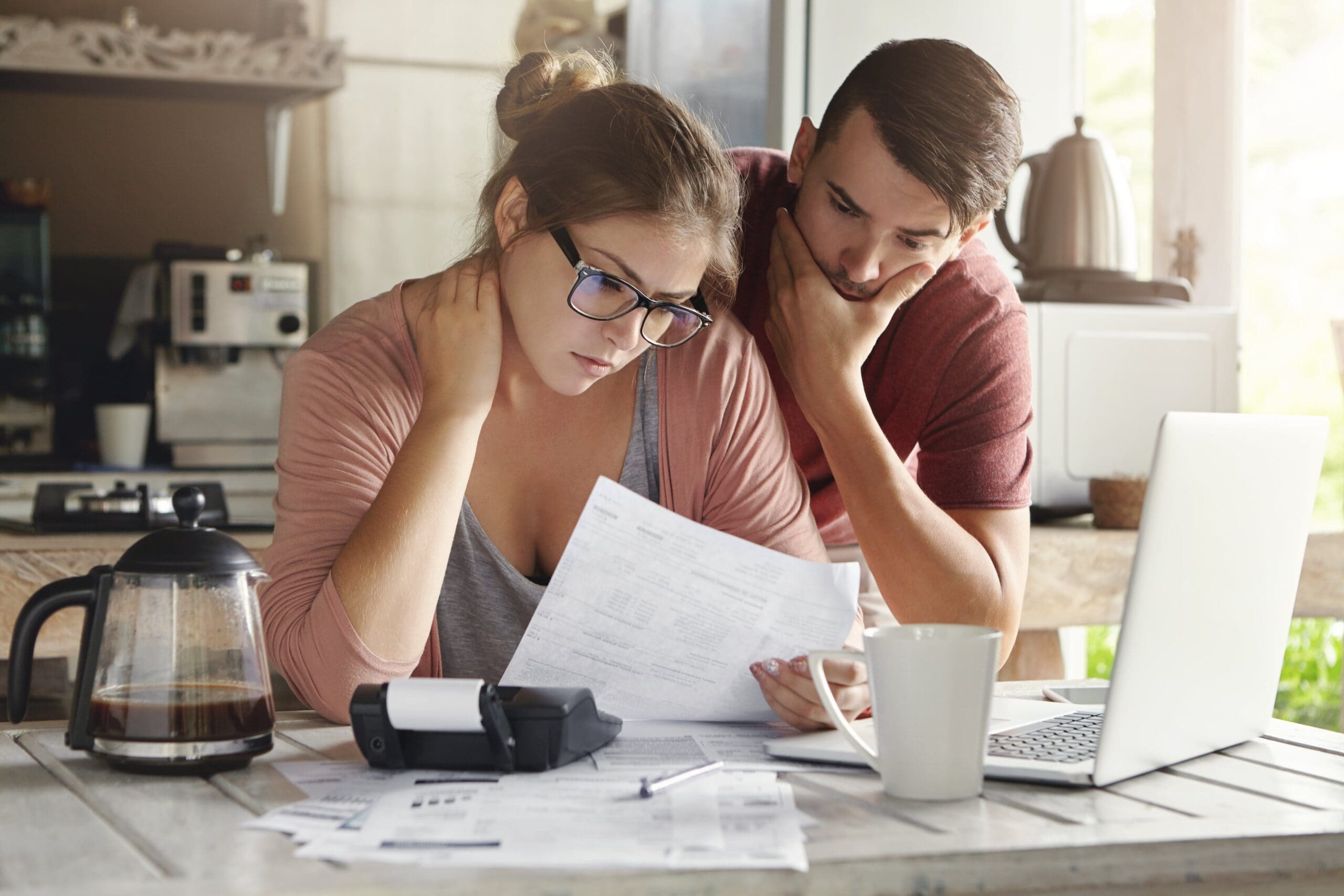 Stressed couple reviewing finances and bills at kitchen table with laptop and calculator