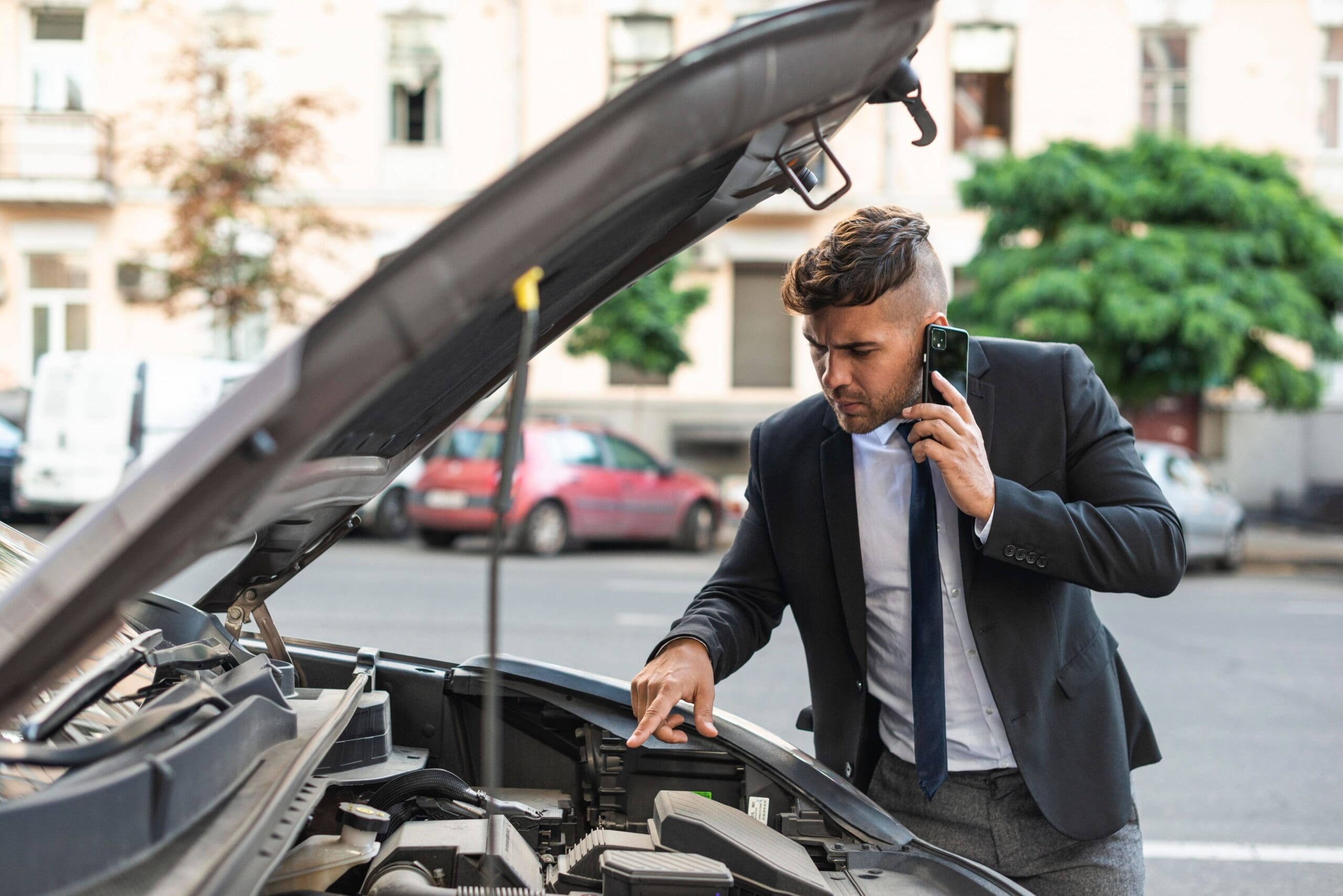 Businessman with broken down car on phone, calling for roadside assistance in the city